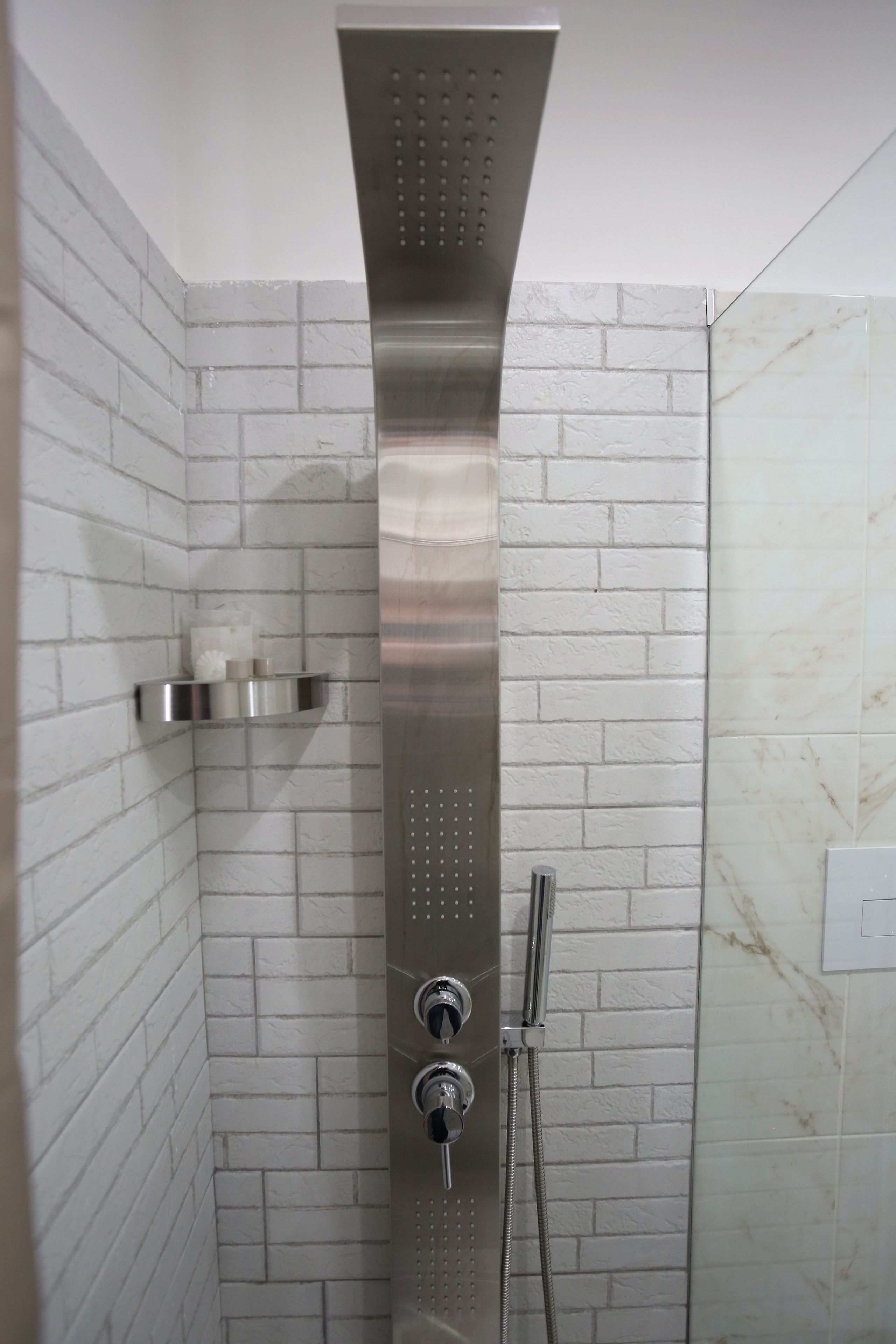 A shower with a modern design, featuring a vertical control panel and a handheld showerhead.