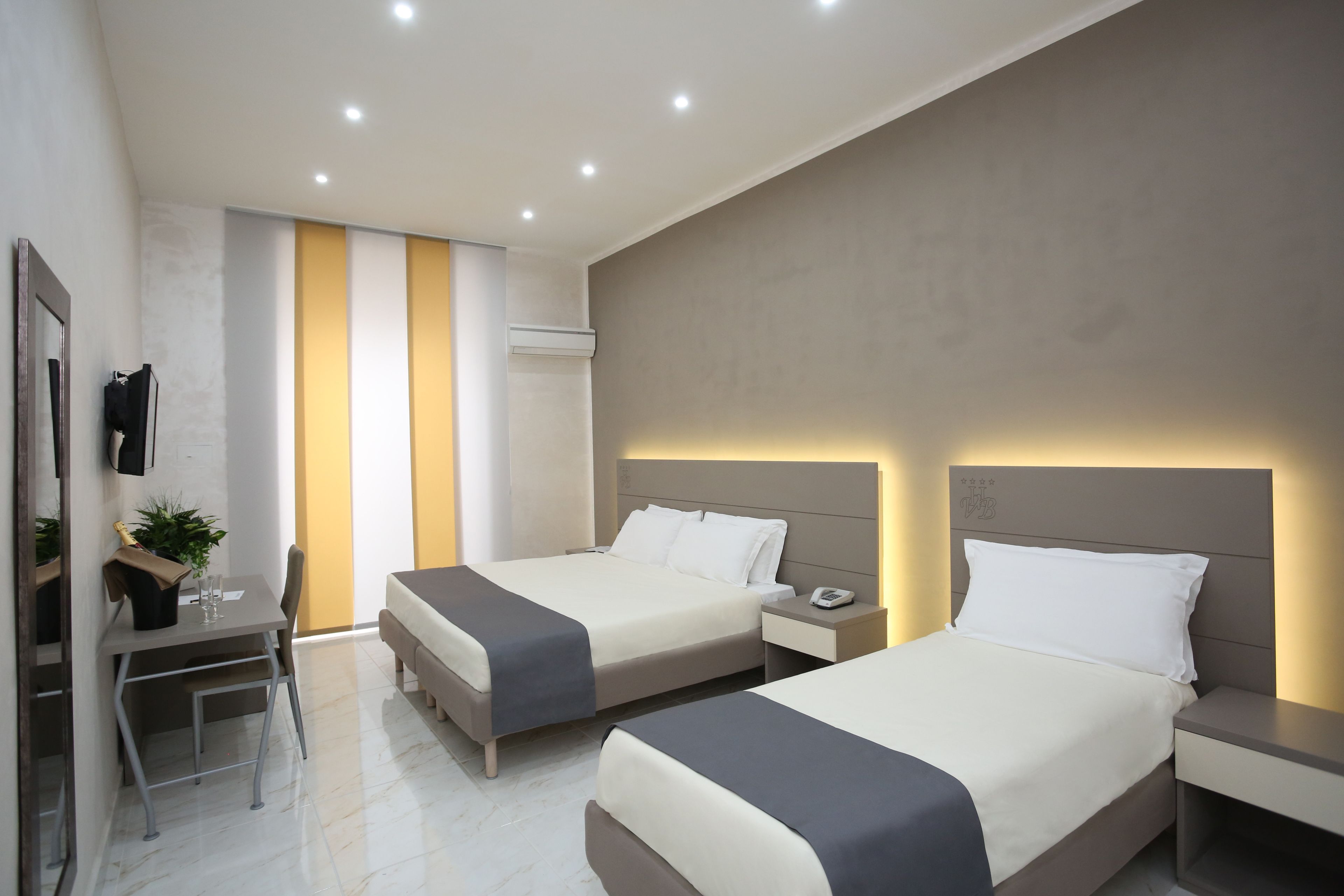 A modern hotel room with two beds, a desk, and a TV.