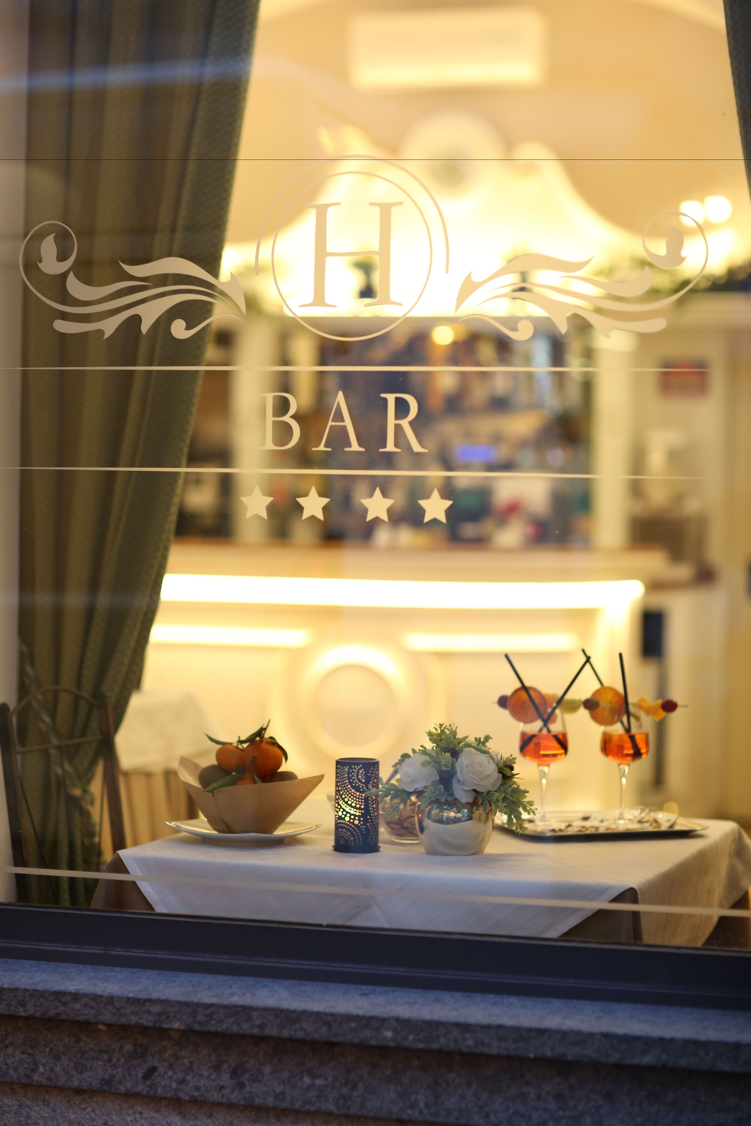 A bar with a decorative sign, a table with a bowl of fruit, a vase with flowers, and a candle holder.