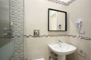 Une salle de bain avec une douche à parois de verre, un lavabo avec un miroir au-dessus et un sèche-cheveux fixé au mur.