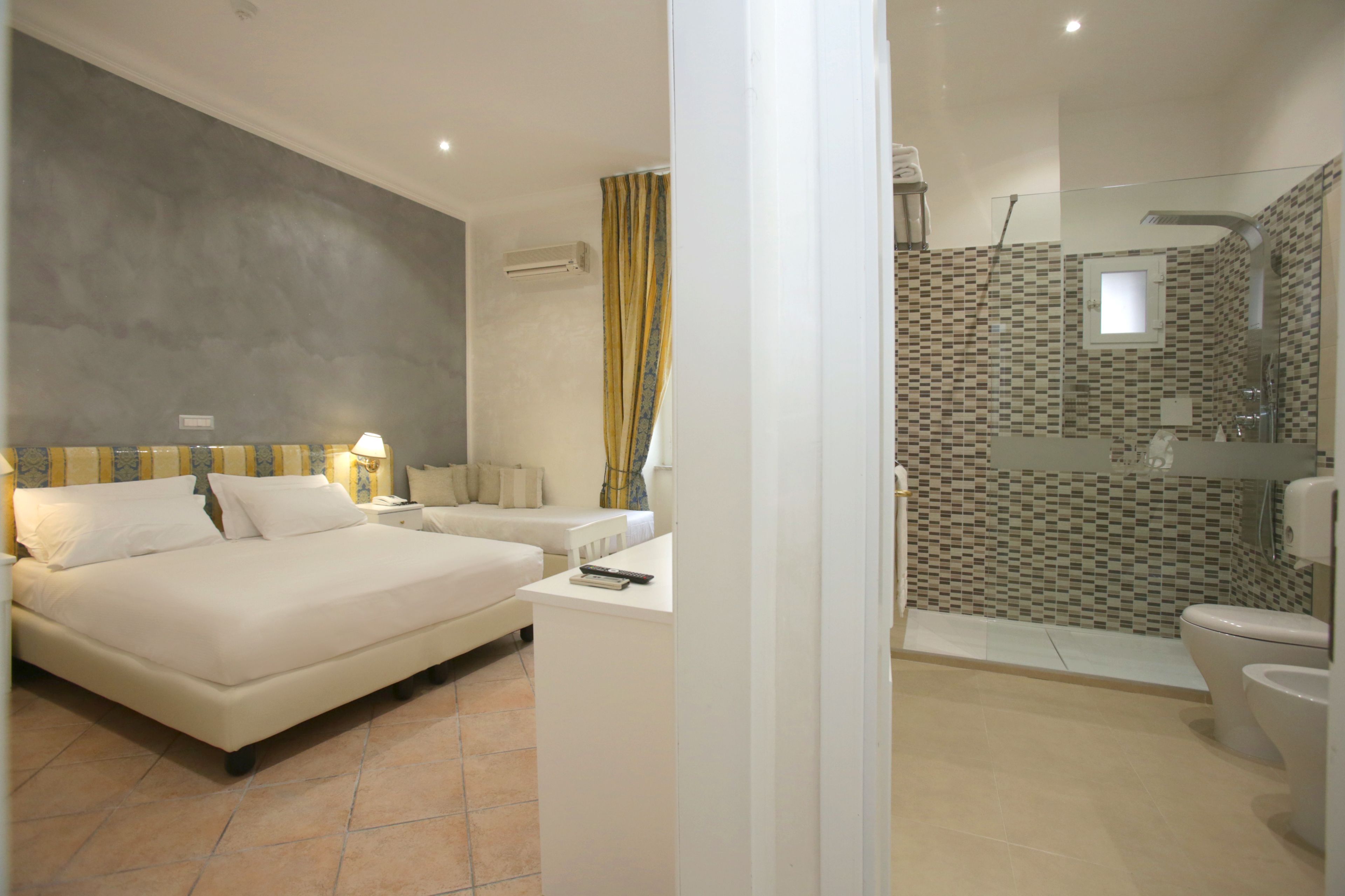 Une chambre avec un grand lit, des tables de chevet et une commode. La salle de bain est équipée d’une douche, de toilettes et d’un lavabo.