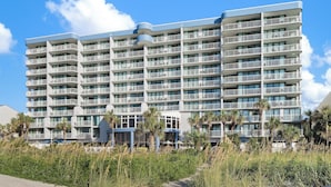 A multi-story hotel with balconies, a beach view, and palm trees.