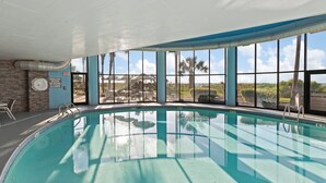 An indoor swimming pool with clear glass walls, a view of the outdoors, and a sign indicating shallow water.