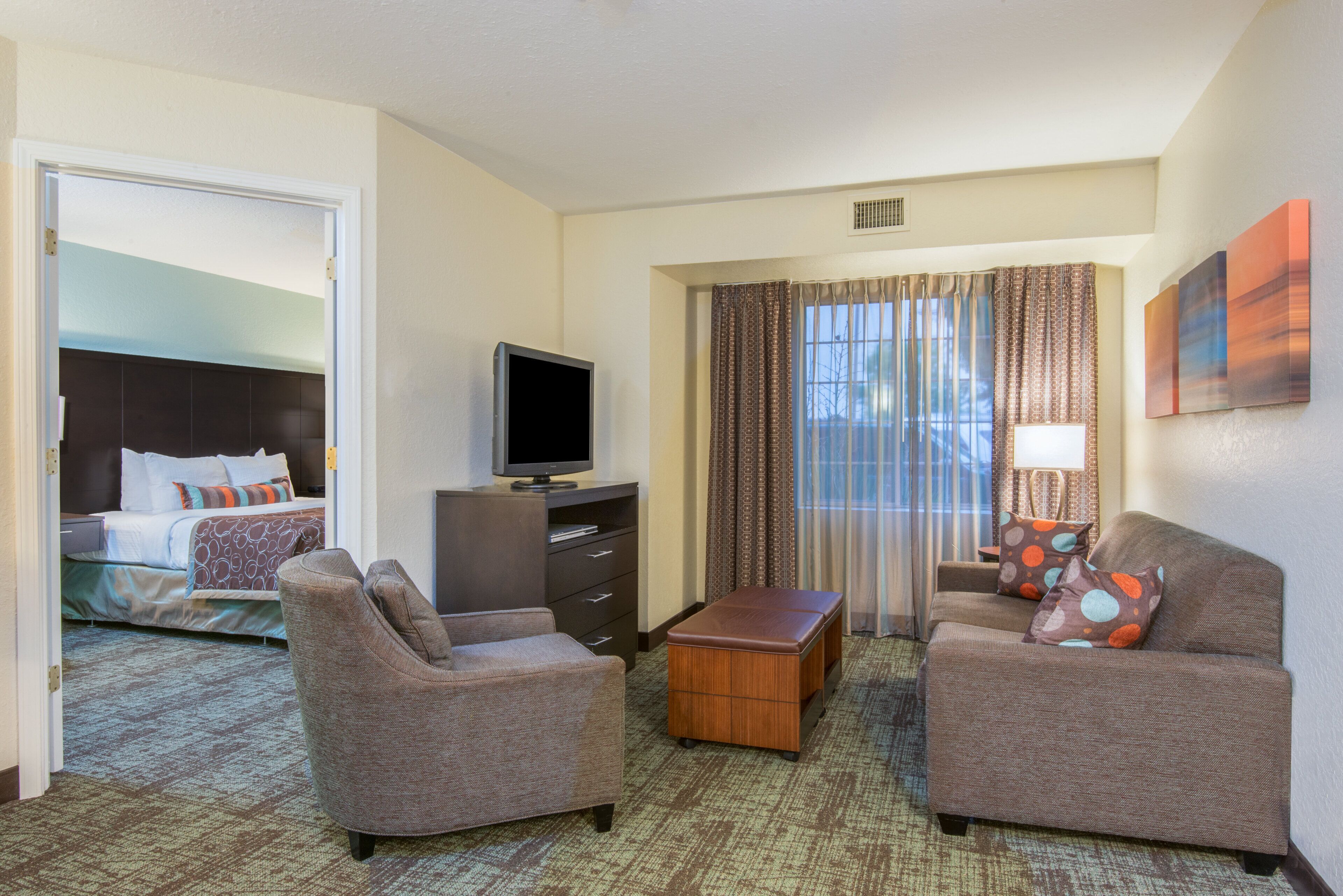A hotel room with a bed, two armchairs, a coffee table, a television, and a window with curtains.