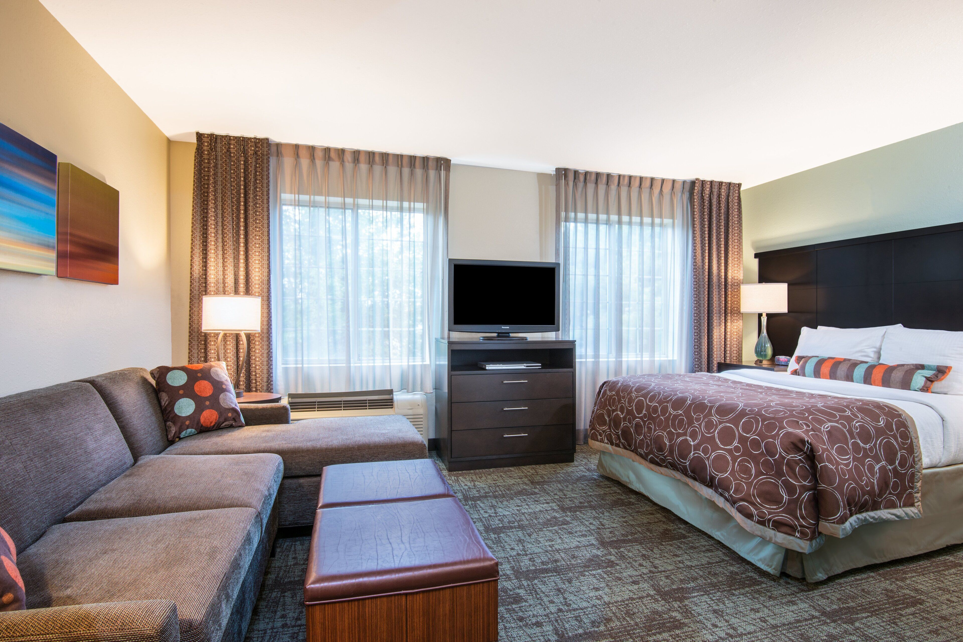 Habitación de hotel con sofá, cama, televisión y escritorio con cajones.