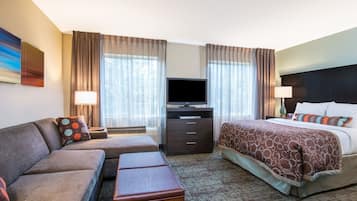Habitación de hotel con sofá, cama, televisión y escritorio con cajones.