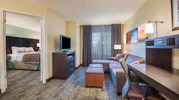 A hotel room with a bed, a desk, a television, a sofa, and a large window with curtains.