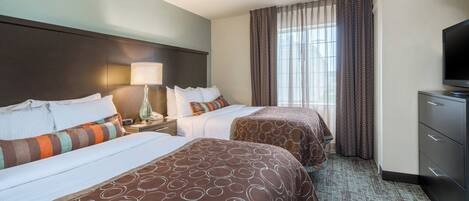 A hotel room with two beds, a nightstand, a lamp, a television, and a large window with curtains.