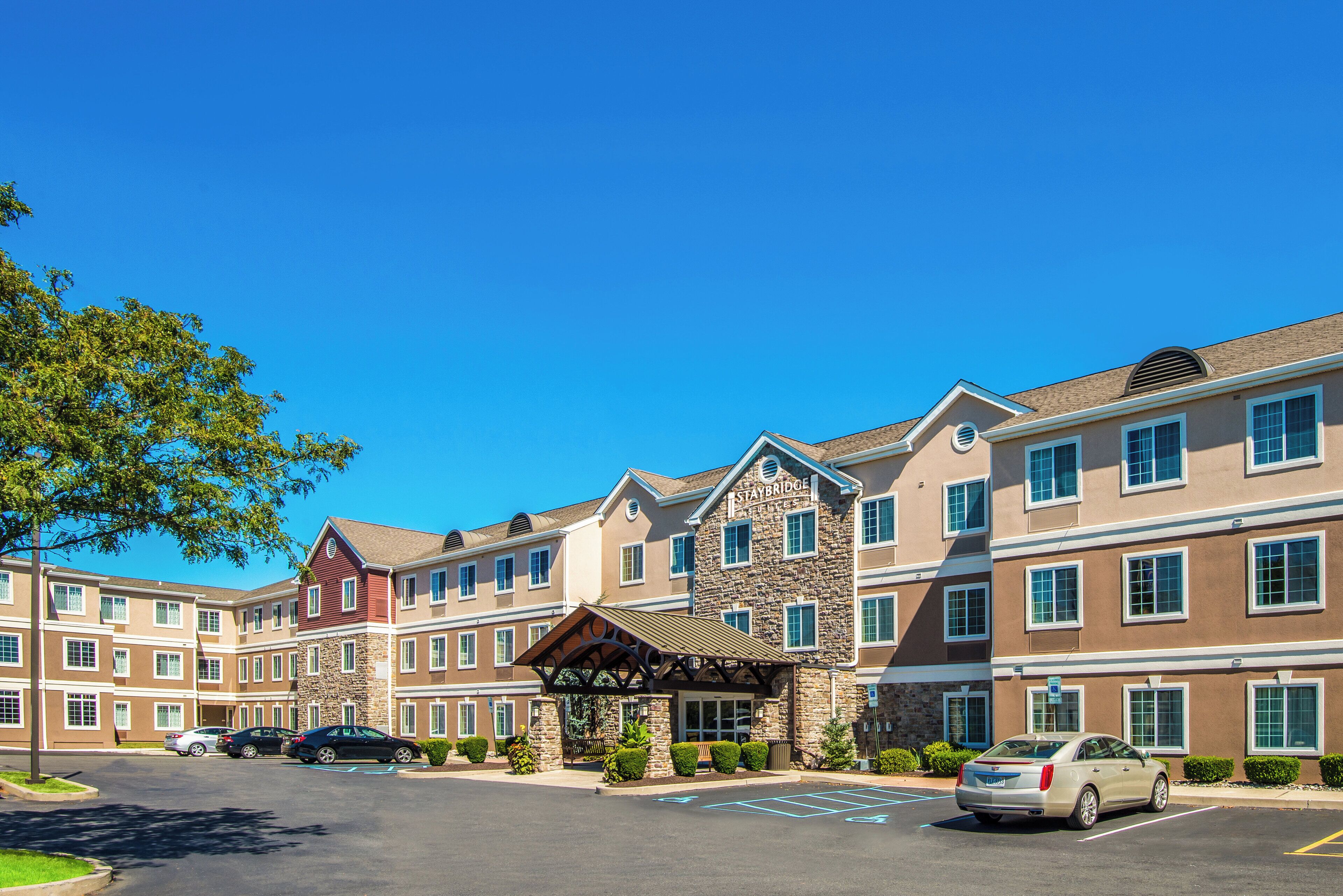 A multi-story hotel with a stone facade, a covered entrance, and a parking lot with cars.