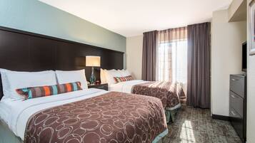 A hotel room with two beds, a nightstand, a lamp, a dresser, and a large window with curtains.