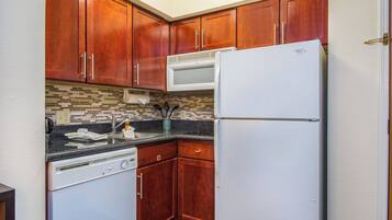 Cocina funcional con armarios de madera, refrigerador blanco, microondas y lavavajillas.