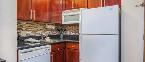Cocina funcional con armarios de madera, refrigerador blanco, microondas y lavavajillas.
