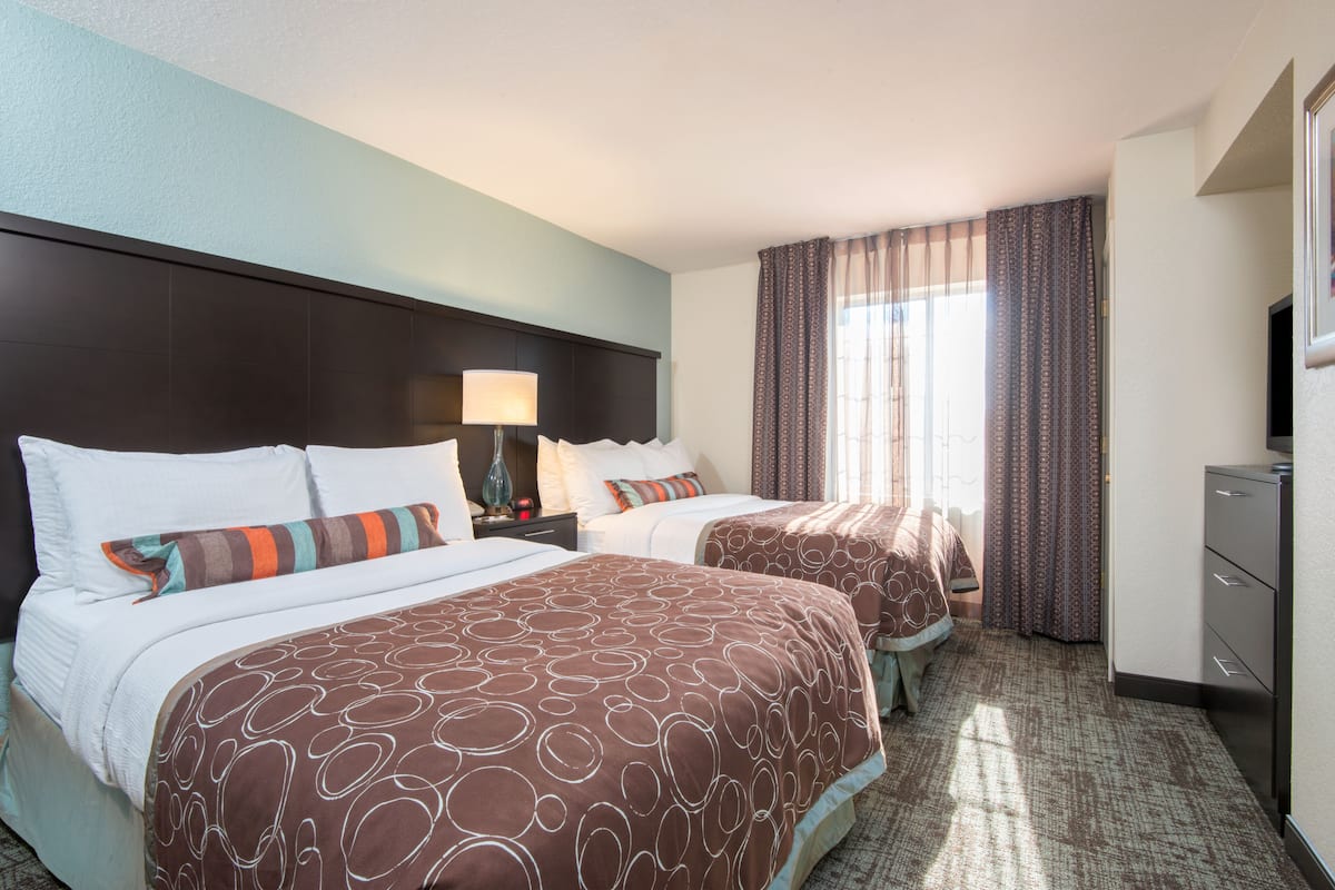 Une chambre d’hôtel avec deux lits, une tête de lit, une table de chevet avec une lampe, une commode et un téléviseur.