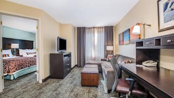 Habitación de hotel con cama, escritorio, silla, televisión, teléfono y ventana con cortinas.