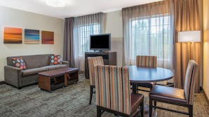 A hotel room with a sofa, a coffee table, a TV, a dining table with chairs, and curtains.