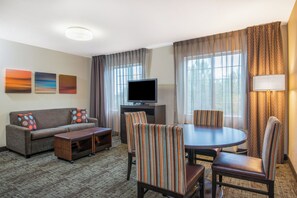 A hotel room with a sofa, a coffee table, a TV, a dining table with chairs, and curtains.