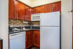 A compact kitchen with wooden cabinets, a built-in microwave, and a dishwasher. - Staybridge Suites Allentown West by IHG (Allentown)