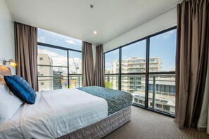 A hotel room with a large bed, a view of the city through floor-to-ceiling windows, and a modern design. - Quest On Nelson (Auckland)