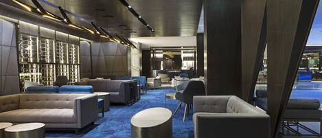 A modern lounge area with sofas, round tables, and a blue carpet.