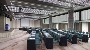 A conference room with rows of chairs, a stage, and a high ceiling with a geometric pattern.