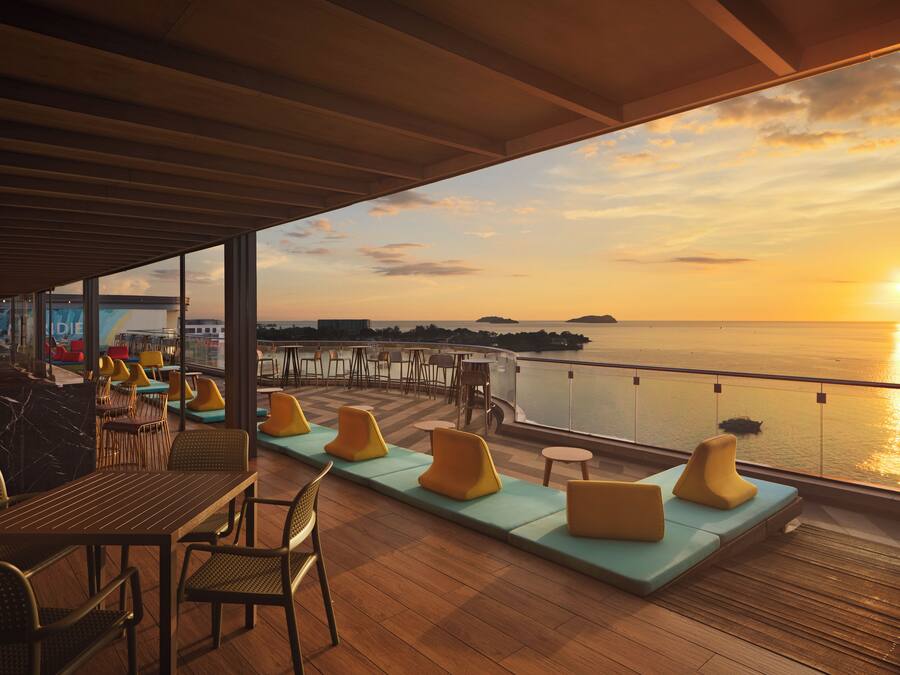 A deck with seating and tables, overlooking a body of water during sunset.