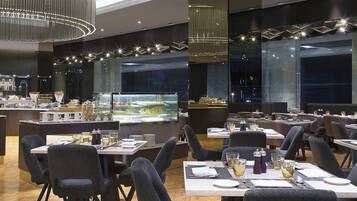 A modern restaurant with a central bar area, multiple dining tables with chairs, and a large display case in the background.