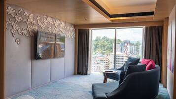 A modern hotel room with a large window, a flat-screen TV mounted on the wall, a sofa with cushions, and a patterned floor.