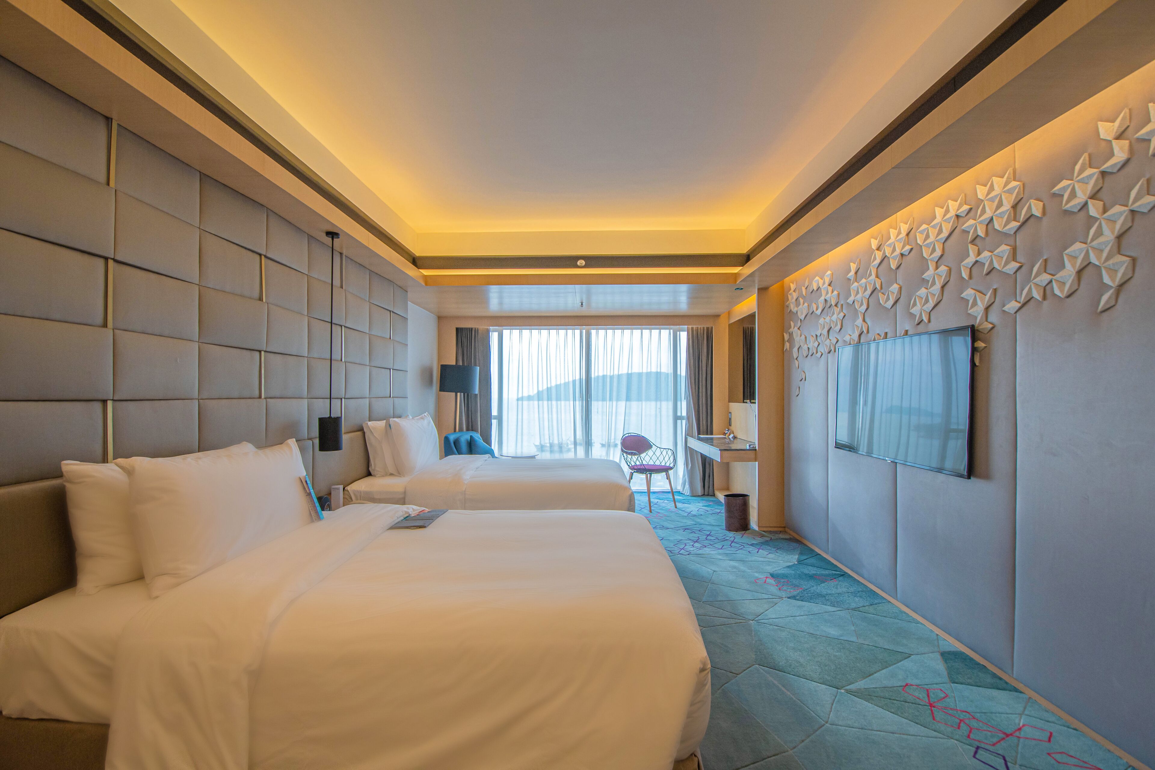 A hotel room with two beds, a desk, a chair, and a large window.