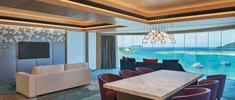 Un moderno cuarto de hotel con un ventanal que ofrece vista al mar, techo de madera, una mesa de mármol y un sofá.