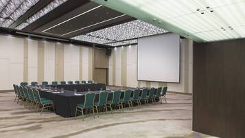 Un salón de conferencias con una larga mesa, sillas, una pantalla de proyector y suelo alfombrado.