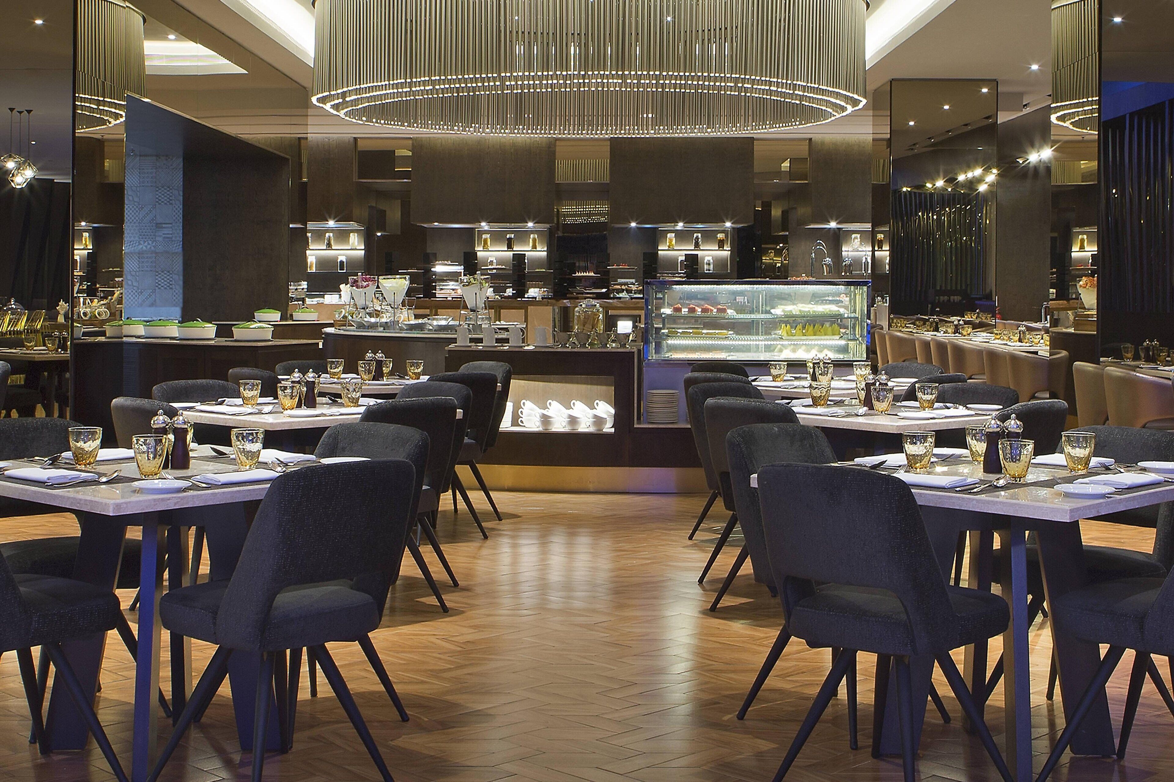 Un restaurante con mesas dispuestas para comer, un mostrador central de postres e iluminación moderna.