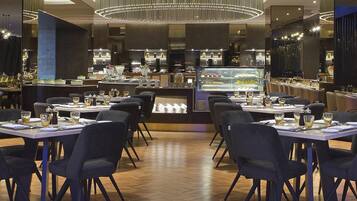 Un restaurante con mesas dispuestas para comer, un mostrador central de postres e iluminación moderna.