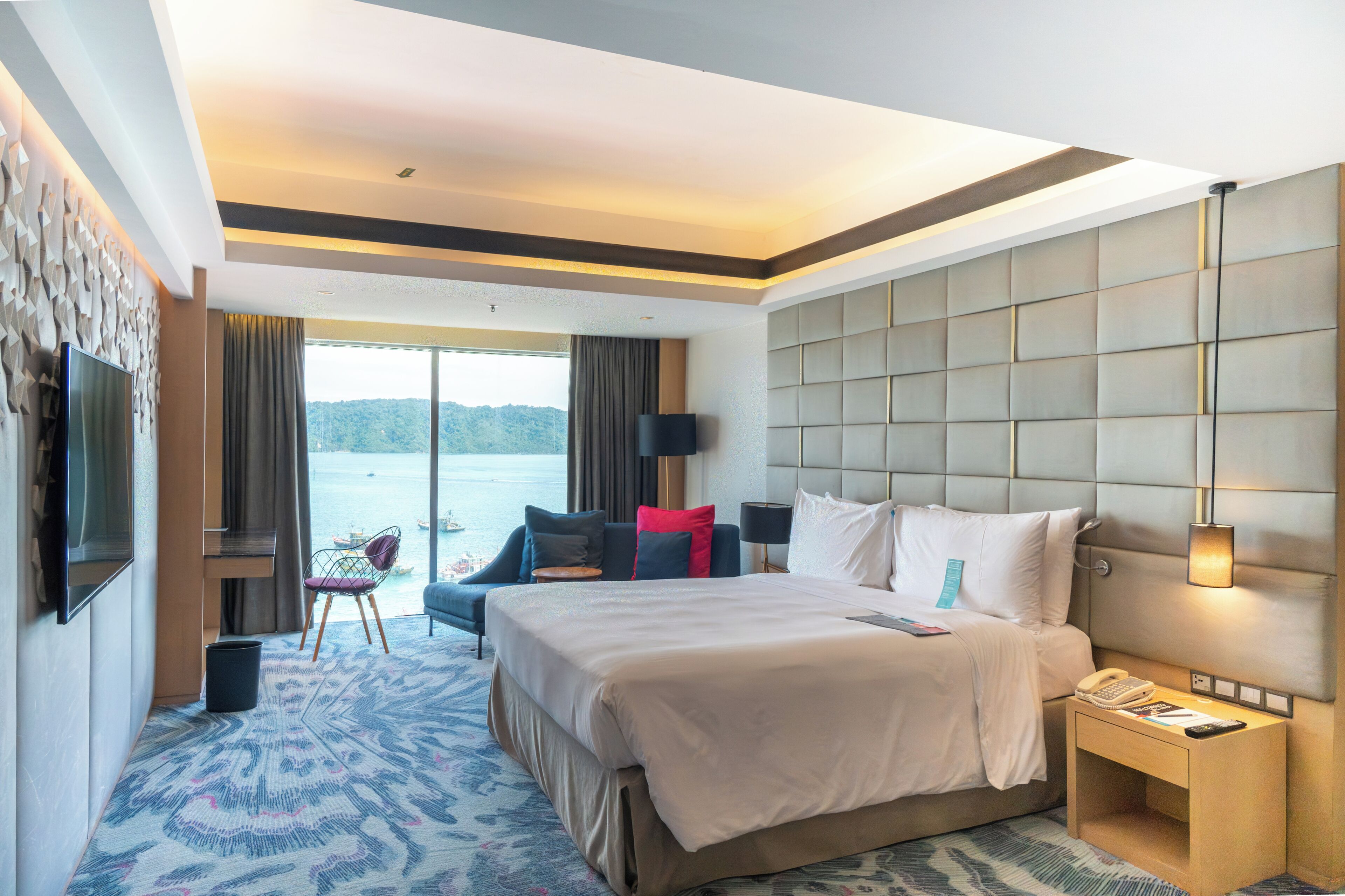 Habitación de hotel con una cama grande, televisión, escritorio, silla y vista al agua.
