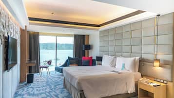 Habitación de hotel con una cama grande, televisión, escritorio, silla y vista al agua.