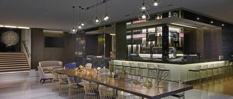 A modern bar area with a long counter, multiple bar stools, and hanging pendant lights.