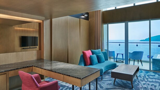 A modern room with a wooden desk, a TV mounted on the wall, a sofa with colorful cushions, and a view of the sea through large windows. - Le Meridien Kota Kinabalu (Kota Kinabalu)