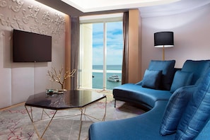 A modern hotel room with a large window, a flat-screen TV, a blue sofa, a glass coffee table, and a decorative wall piece. - Le Meridien Kota Kinabalu (Kota Kinabalu)