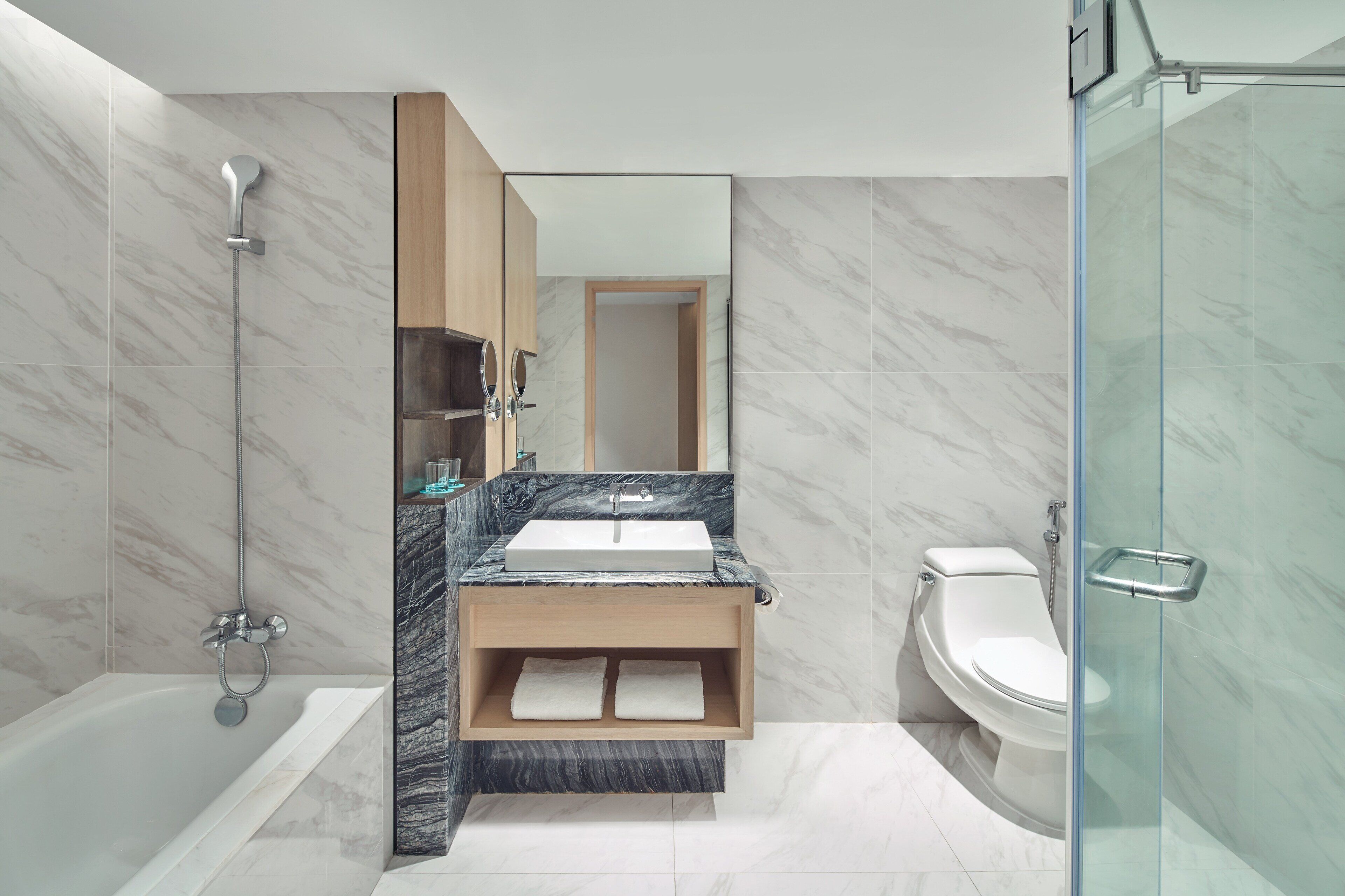 A modern bathroom with a bathtub, a sink with a marble countertop, a toilet, and a glass shower enclosure.