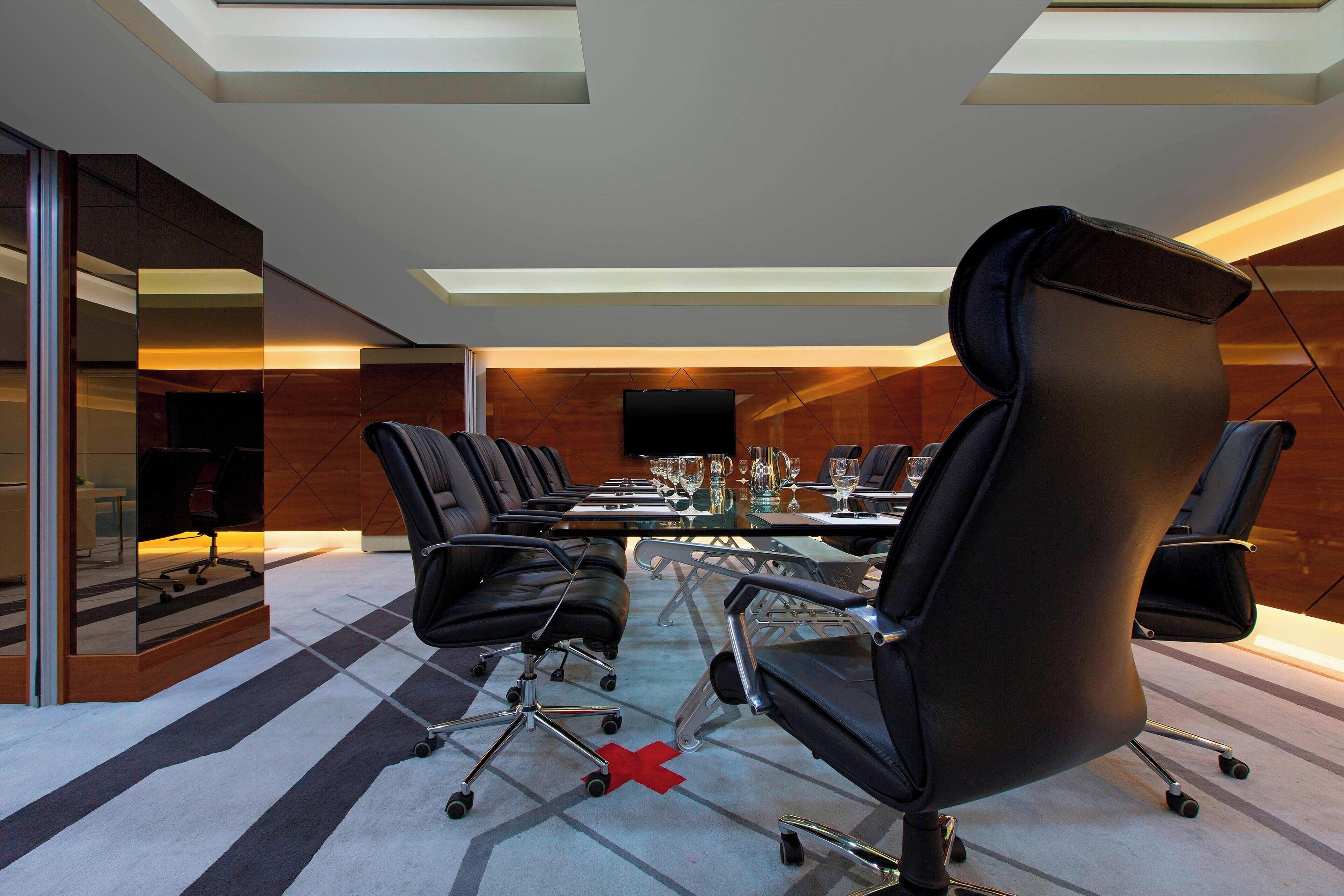 A modern conference room with a glass table, black leather chairs, and a large screen.