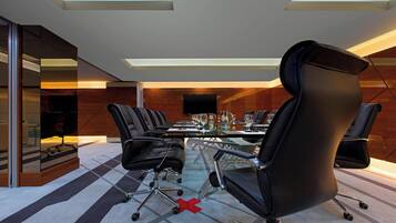 A modern conference room with a glass table, black leather chairs, and a large screen.