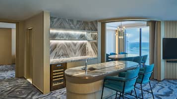 A modern kitchen with a marble countertop, bar stools, and a large window offering a view of the sea.