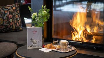 Ein gemütlicher Sitzbereich mit Kamin, einem Tisch mit Speisekarte, einem Croissant und einer Kaffeetasse.