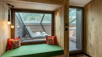 Una habitación acogedora con detalles de madera, un banco tapizado en verde con cojines de colores y un amplio ventanal con vistas a una terraza amueblada.