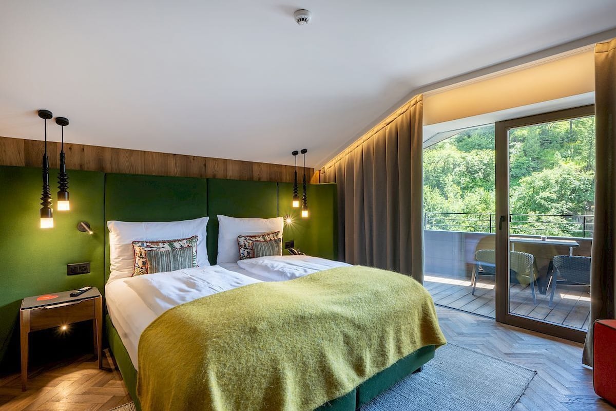 A modern hotel room with a large bed, green walls, and a balcony with outdoor furniture.
