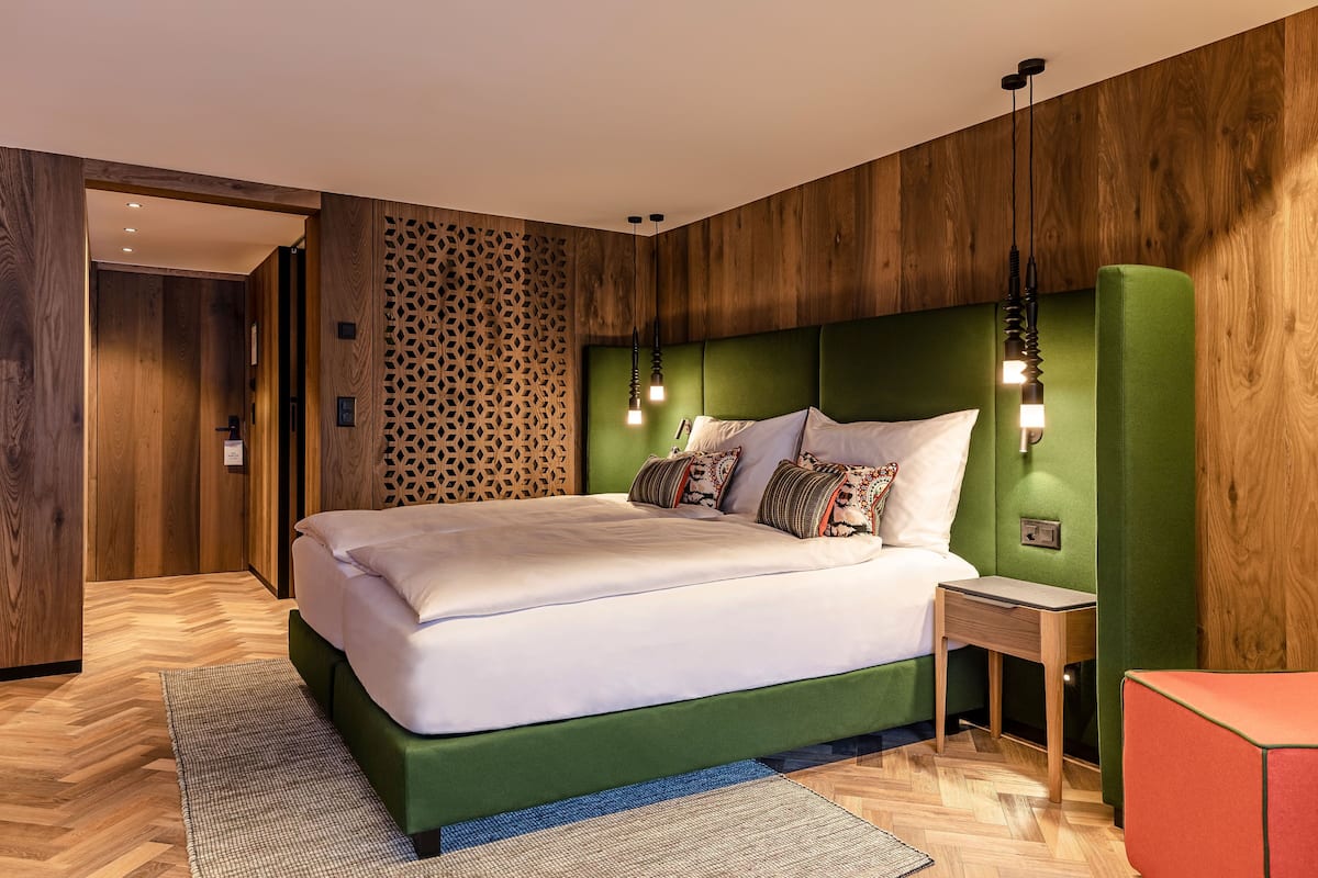 A modern bedroom with a green upholstered headboard, a wooden floor, and a patterned wall.