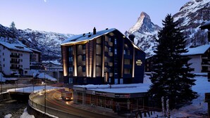 A modern building with a ski resort in the background, a snow-covered landscape, and a road with light trails. - Hotel ZERMAMA Zermatt (Zermatt)