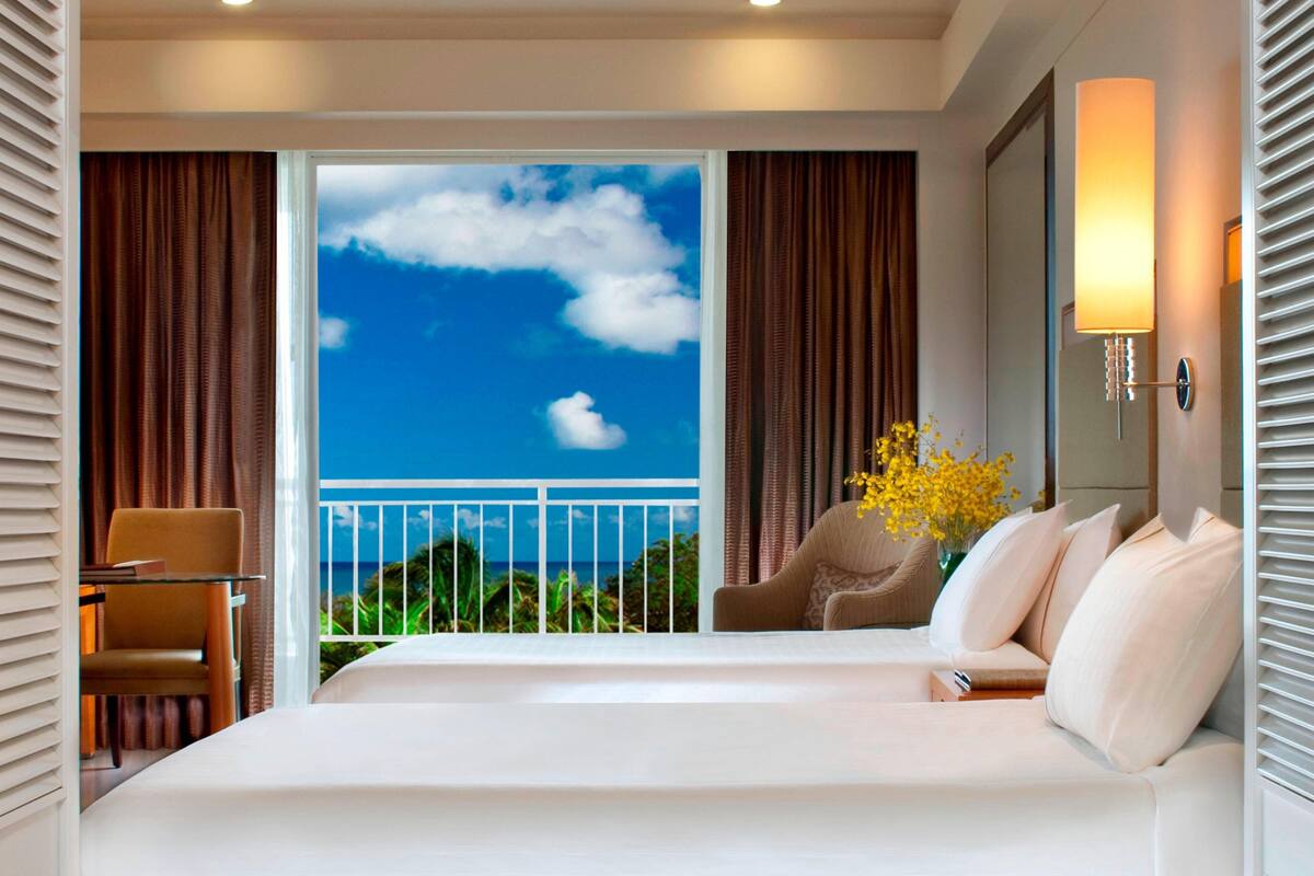 Habitación de hotel con una cama grande, una silla, un escritorio y vista al océano desde un balcón.