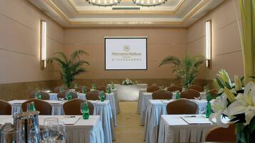 Uma sala de conferências no Sheraton Haikou Resort, com mesas preparadas para uma reunião, arranjos florais e uma tela de projetor exibindo o nome do resort.