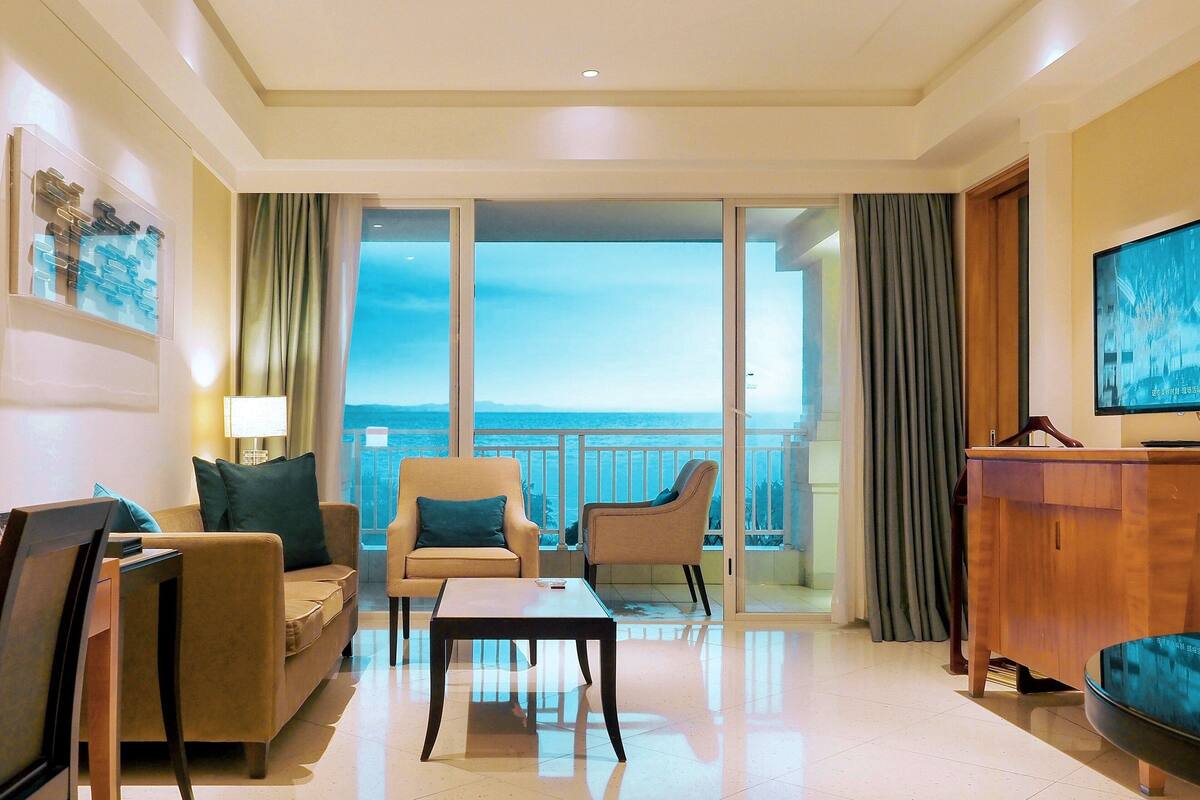 Una habitación de hotel moderna con balcón, un sofá, una silla, una mesa de centro y un televisor.