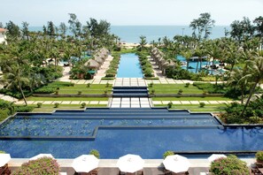 Un resort con piscina central, palmeras y vista al océano.